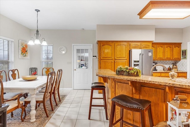 kitchen with stainless steel refrigerator with ice dispenser, a breakfast bar, light tile patterned floors, decorative light fixtures, and a chandelier