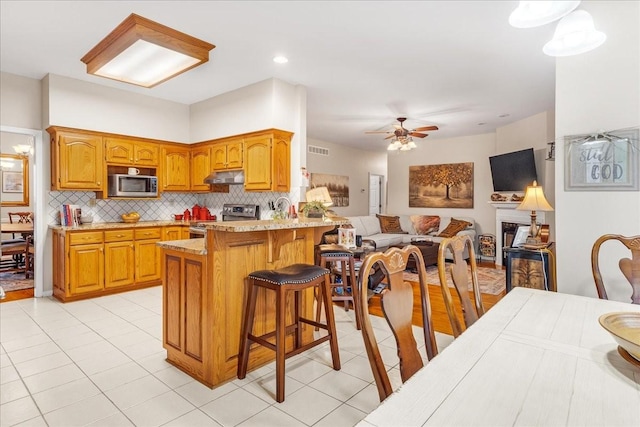 kitchen featuring kitchen peninsula, a kitchen bar, tasteful backsplash, stainless steel appliances, and ceiling fan