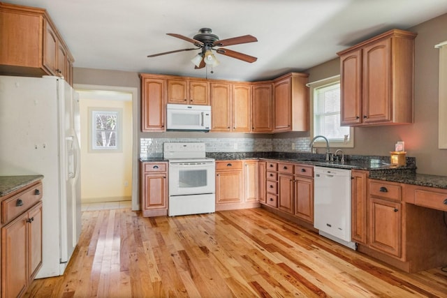 kitchen featuring ceiling fan, sink, dark stone counters, white appliances, and light wood-type flooring