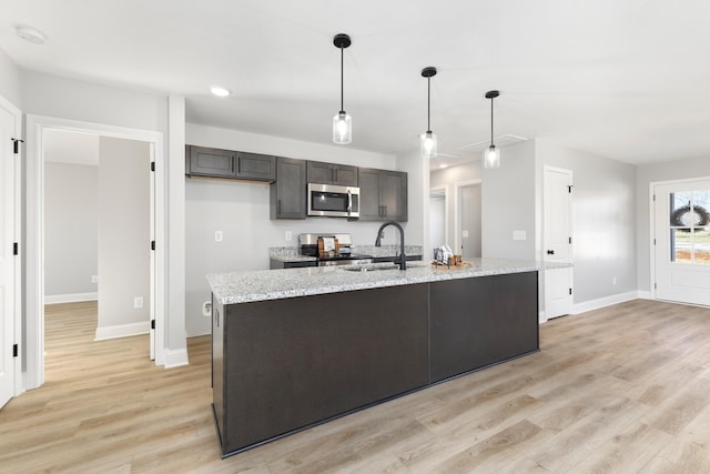 kitchen featuring light stone countertops, stainless steel appliances, hanging light fixtures, and an island with sink