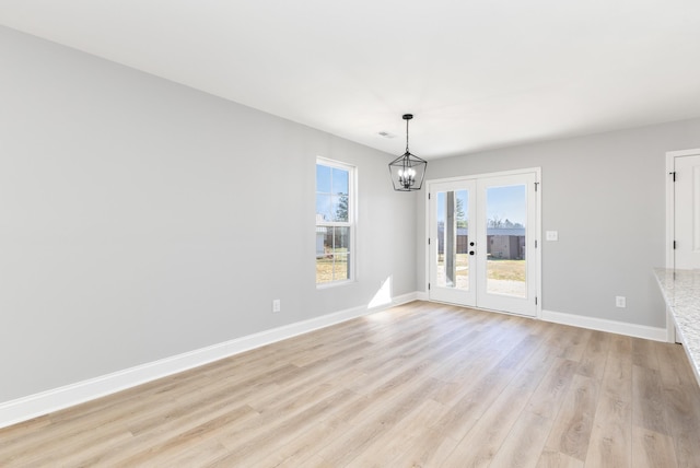 unfurnished dining area with a chandelier, light hardwood / wood-style flooring, and french doors