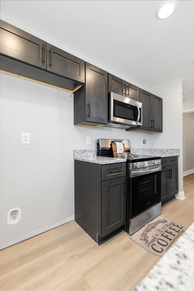 kitchen featuring light hardwood / wood-style floors, light stone counters, dark brown cabinetry, and appliances with stainless steel finishes