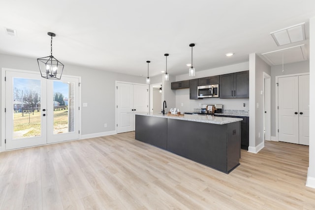 kitchen with appliances with stainless steel finishes, light wood-type flooring, sink, a center island with sink, and hanging light fixtures