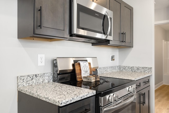 kitchen with light stone counters, light wood-type flooring, and stainless steel appliances