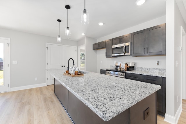 kitchen with dark brown cabinetry, sink, stainless steel appliances, an island with sink, and pendant lighting