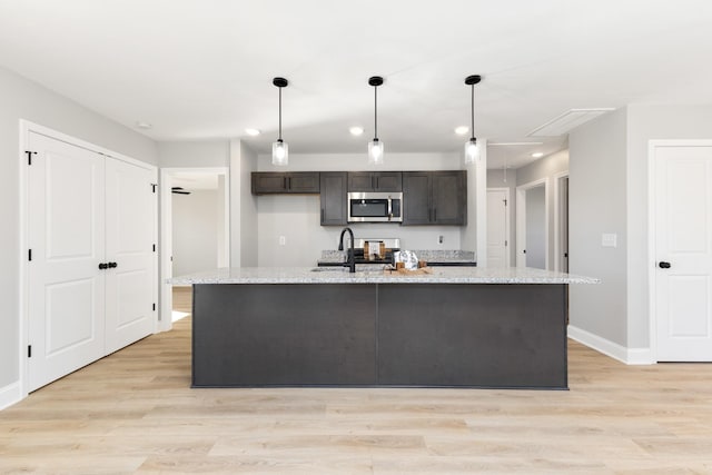 kitchen featuring light stone countertops, stainless steel appliances, hanging light fixtures, and a center island with sink