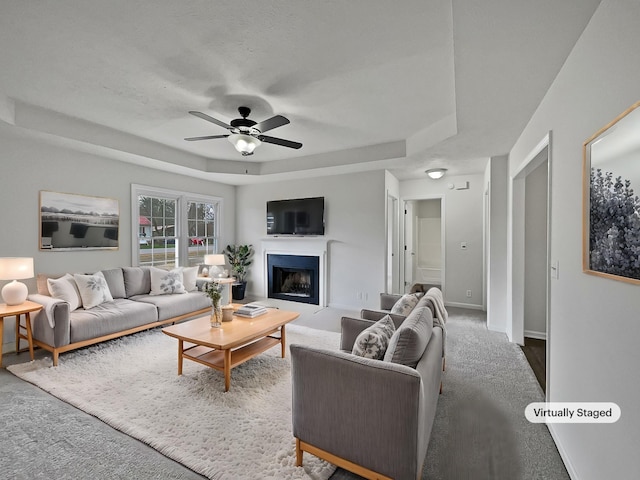 living room with a tray ceiling, ceiling fan, and carpet floors