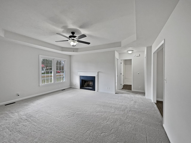 unfurnished living room featuring a tray ceiling, ceiling fan, and carpet floors