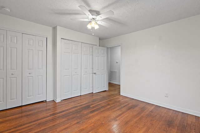 unfurnished bedroom featuring multiple closets, ceiling fan, dark hardwood / wood-style floors, and a textured ceiling