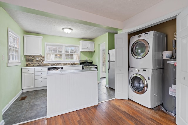 clothes washing area with sink, dark wood-type flooring, water heater, stacked washer and clothes dryer, and a textured ceiling