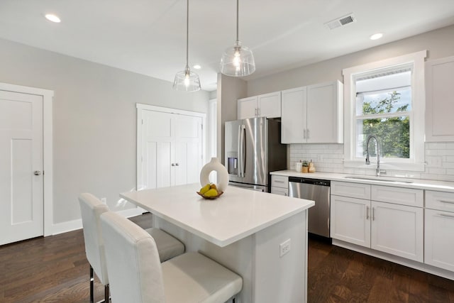 kitchen featuring white cabinetry, sink, decorative light fixtures, a kitchen island, and appliances with stainless steel finishes