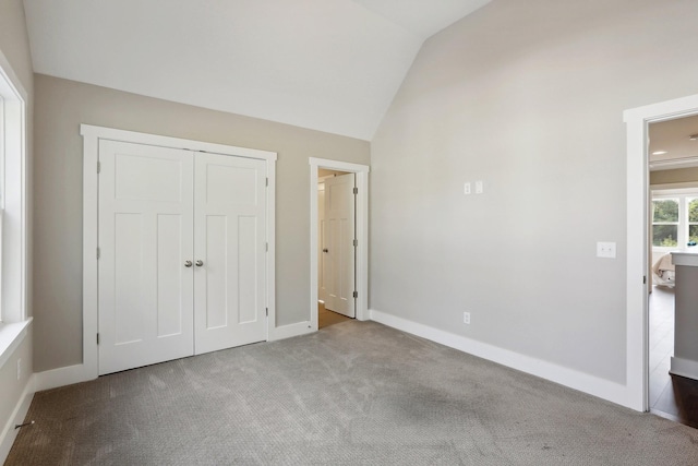 unfurnished bedroom with light colored carpet, a closet, and lofted ceiling