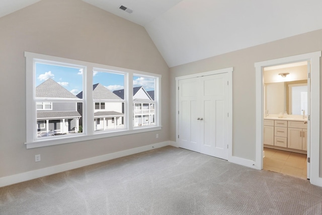 unfurnished bedroom with vaulted ceiling, light carpet, and ensuite bath