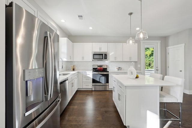 kitchen with decorative light fixtures, stainless steel appliances, white cabinetry, and a breakfast bar area