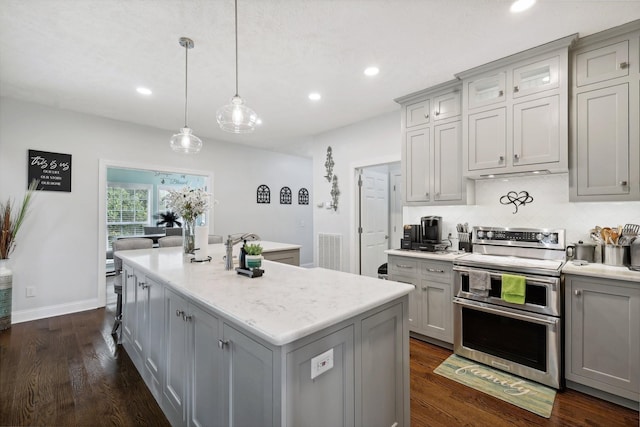 kitchen featuring gray cabinets, a center island with sink, and double oven range