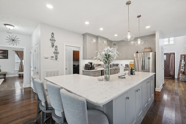 kitchen featuring stainless steel refrigerator, gray cabinetry, dark wood-type flooring, a large island with sink, and pendant lighting