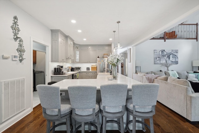 kitchen featuring a kitchen bar, stainless steel fridge, dark wood-type flooring, a spacious island, and decorative light fixtures