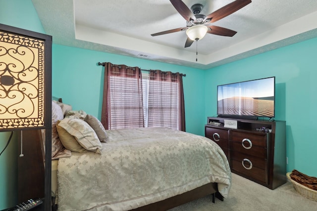 carpeted bedroom with ceiling fan, a raised ceiling, and a textured ceiling