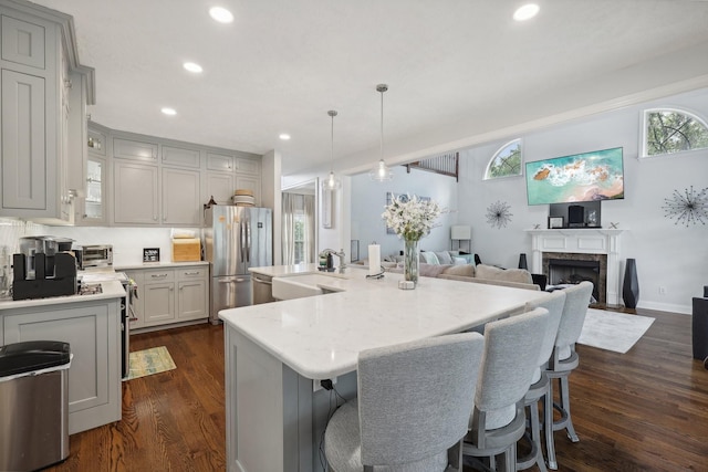 kitchen featuring stove, a kitchen island with sink, dark hardwood / wood-style floors, stainless steel fridge, and decorative light fixtures