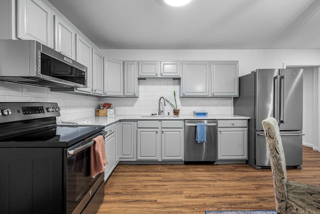 kitchen featuring hardwood / wood-style flooring, appliances with stainless steel finishes, gray cabinetry, tasteful backsplash, and sink