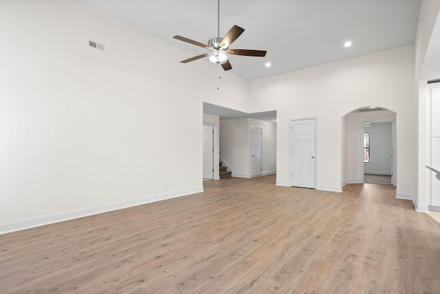 unfurnished living room with ceiling fan, a towering ceiling, and light wood-type flooring