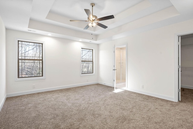 unfurnished bedroom with ceiling fan, ensuite bathroom, a tray ceiling, and a walk in closet