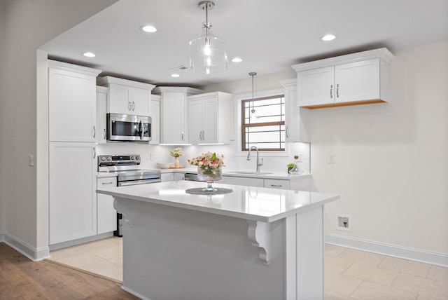 kitchen featuring decorative light fixtures, a kitchen island, sink, appliances with stainless steel finishes, and white cabinets