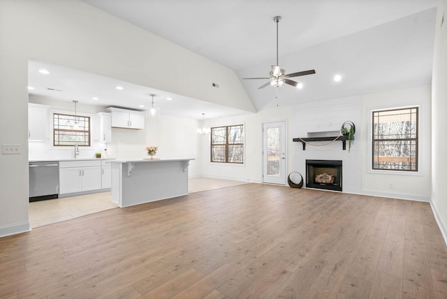 unfurnished living room with vaulted ceiling, a fireplace, sink, ceiling fan, and light hardwood / wood-style flooring