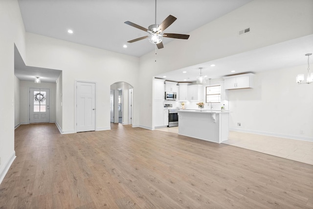 unfurnished living room with high vaulted ceiling, ceiling fan with notable chandelier, and light wood-type flooring