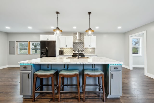 kitchen featuring pendant lighting, black refrigerator with ice dispenser, white cabinets, a spacious island, and wall chimney range hood