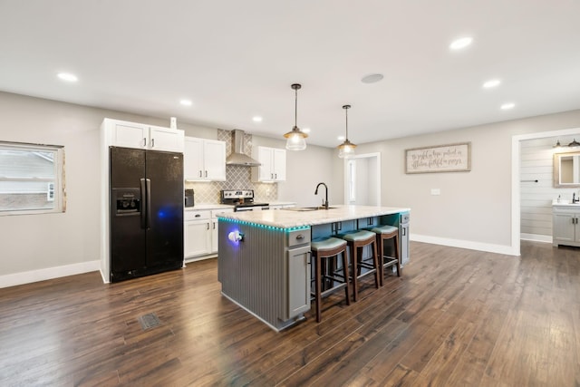 kitchen with white cabinets, wall chimney exhaust hood, an island with sink, and black refrigerator with ice dispenser