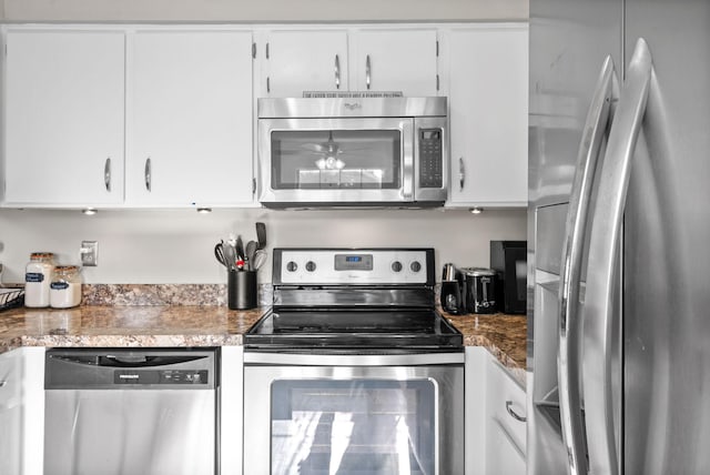 kitchen with white cabinetry, stainless steel appliances, and dark stone counters