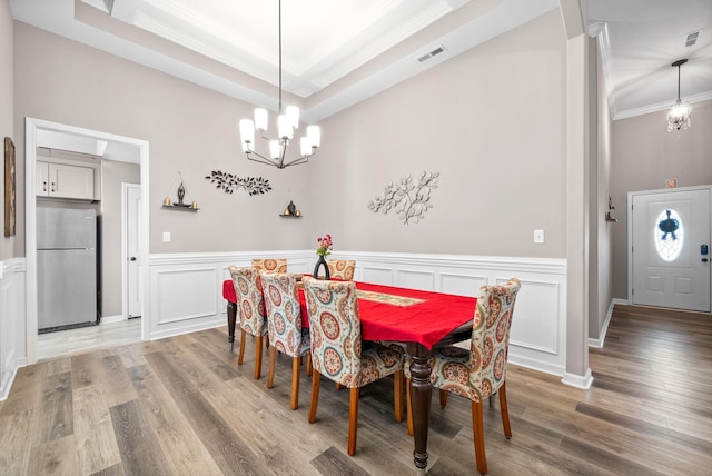 dining area featuring a tray ceiling, light hardwood / wood-style flooring, a notable chandelier, and ornamental molding