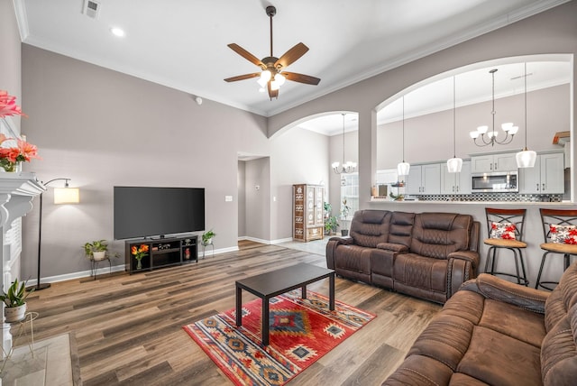 living room featuring ceiling fan with notable chandelier, hardwood / wood-style flooring, crown molding, and a tiled fireplace