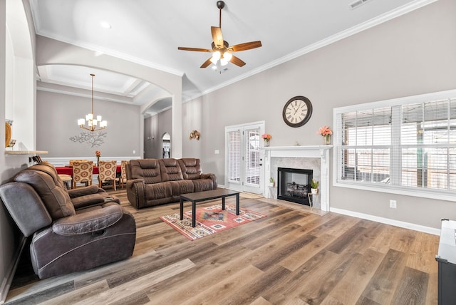 living room featuring ceiling fan with notable chandelier, wood-type flooring, crown molding, and a high end fireplace