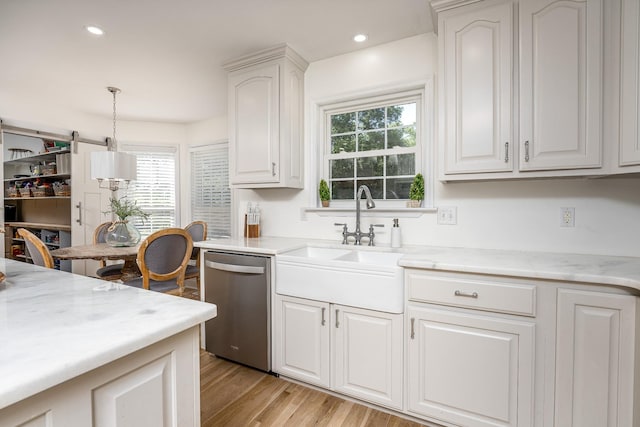 kitchen with sink, light hardwood / wood-style flooring, stainless steel dishwasher, decorative light fixtures, and white cabinetry