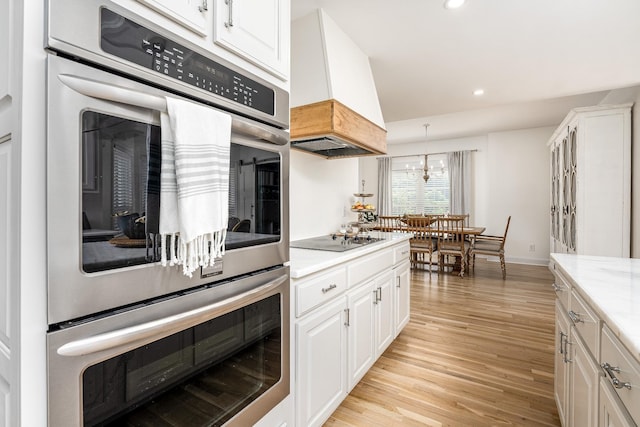 kitchen with white cabinetry, light stone counters, double oven, black electric stovetop, and custom exhaust hood