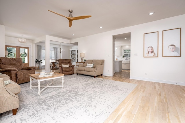 living room featuring french doors, ceiling fan with notable chandelier, and light hardwood / wood-style flooring