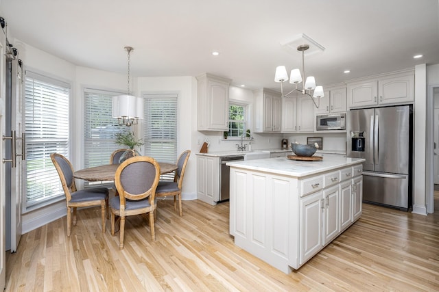 kitchen featuring white cabinets, light wood-type flooring, appliances with stainless steel finishes, decorative light fixtures, and a kitchen island