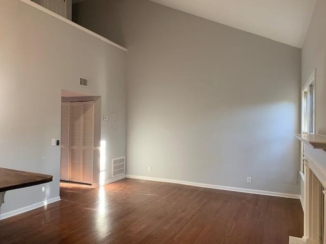 unfurnished living room with high vaulted ceiling and dark wood-type flooring