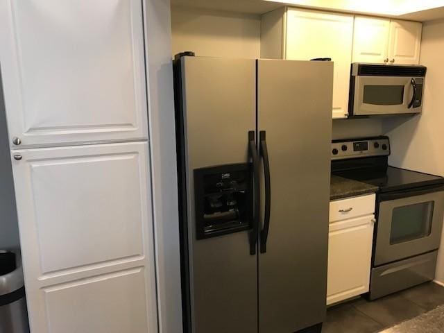 kitchen with white cabinets, dark tile patterned flooring, and appliances with stainless steel finishes