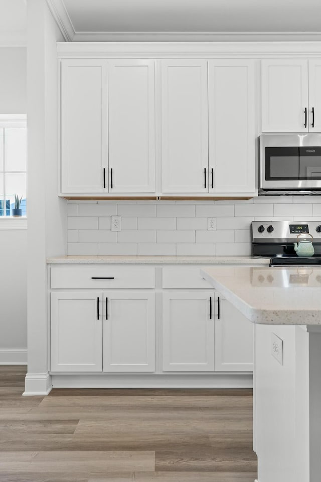 kitchen with white cabinets, light wood-type flooring, backsplash, and appliances with stainless steel finishes