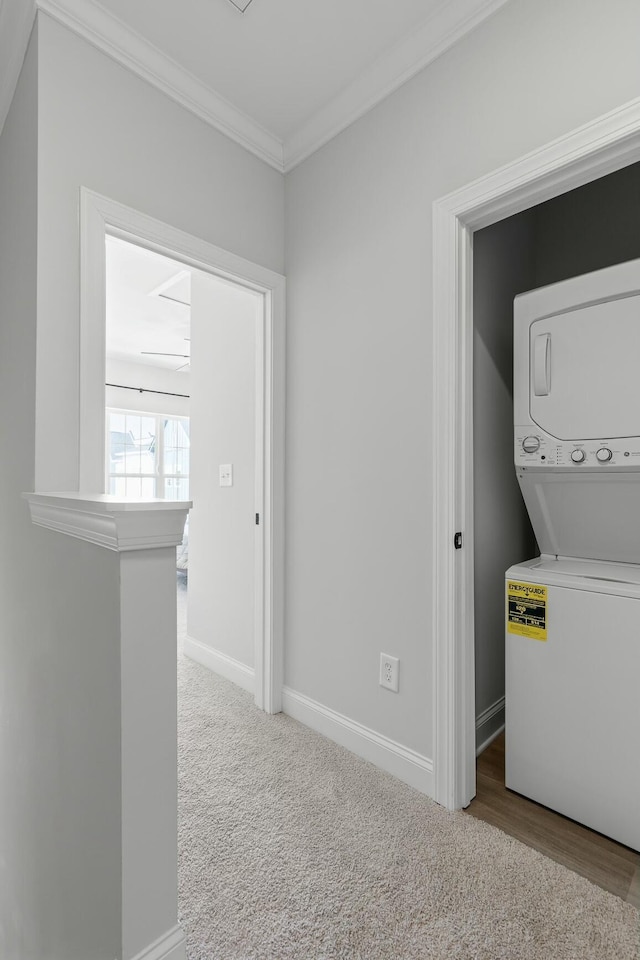 clothes washing area featuring light colored carpet, crown molding, and stacked washer / drying machine