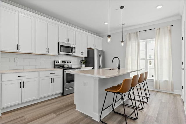 kitchen with appliances with stainless steel finishes, a kitchen island with sink, sink, pendant lighting, and white cabinetry