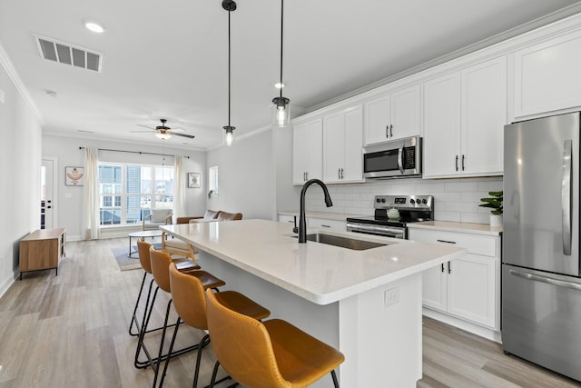 kitchen with decorative backsplash, appliances with stainless steel finishes, a center island with sink, decorative light fixtures, and white cabinetry