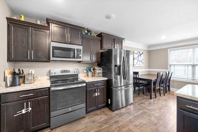 kitchen with dark brown cabinetry, crown molding, stainless steel appliances, and hardwood / wood-style flooring