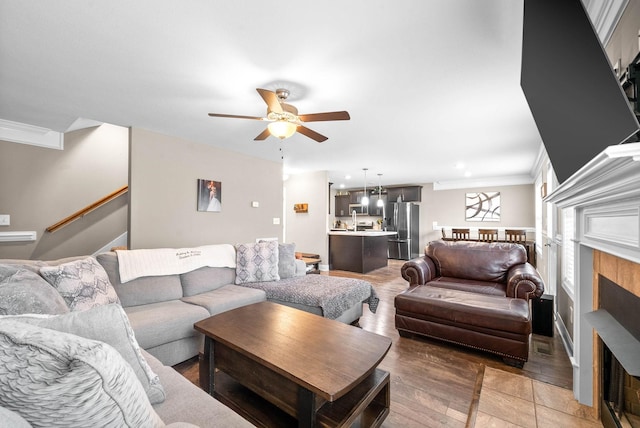 living room featuring ceiling fan, crown molding, wood-type flooring, and a fireplace