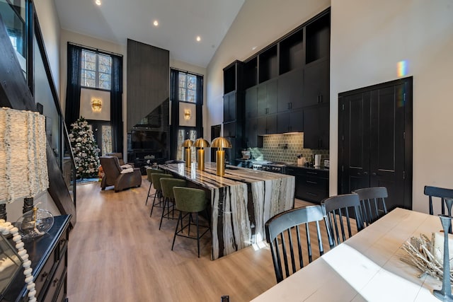 kitchen with a breakfast bar area, high vaulted ceiling, decorative backsplash, a fireplace, and light hardwood / wood-style flooring