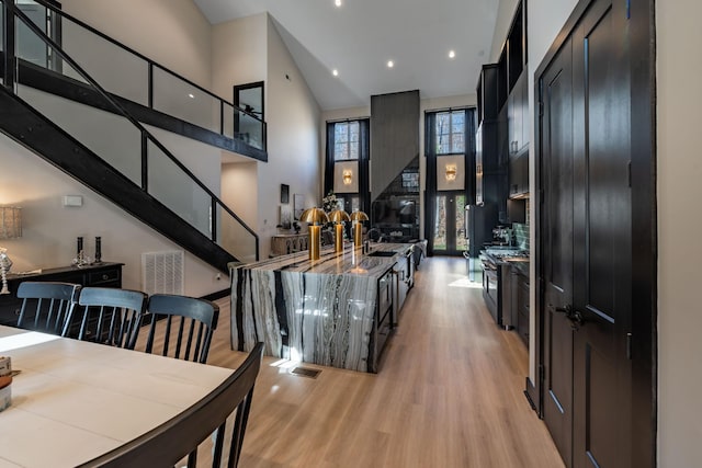 kitchen with light hardwood / wood-style flooring, a towering ceiling, stone counters, stainless steel range with gas stovetop, and sink