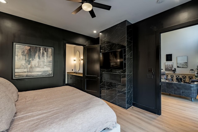 bedroom with ensuite bath, a premium fireplace, ceiling fan, and light hardwood / wood-style floors